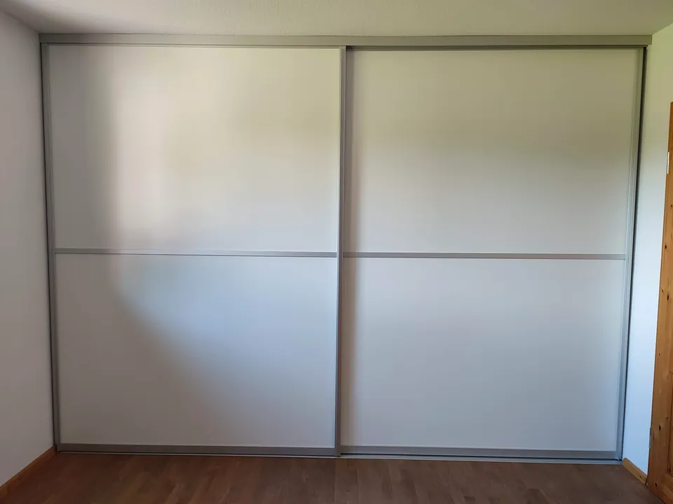 Raumhoher Einbauschrank mit zwei hellen Schiebetürfronten zwischen zwei Wänden